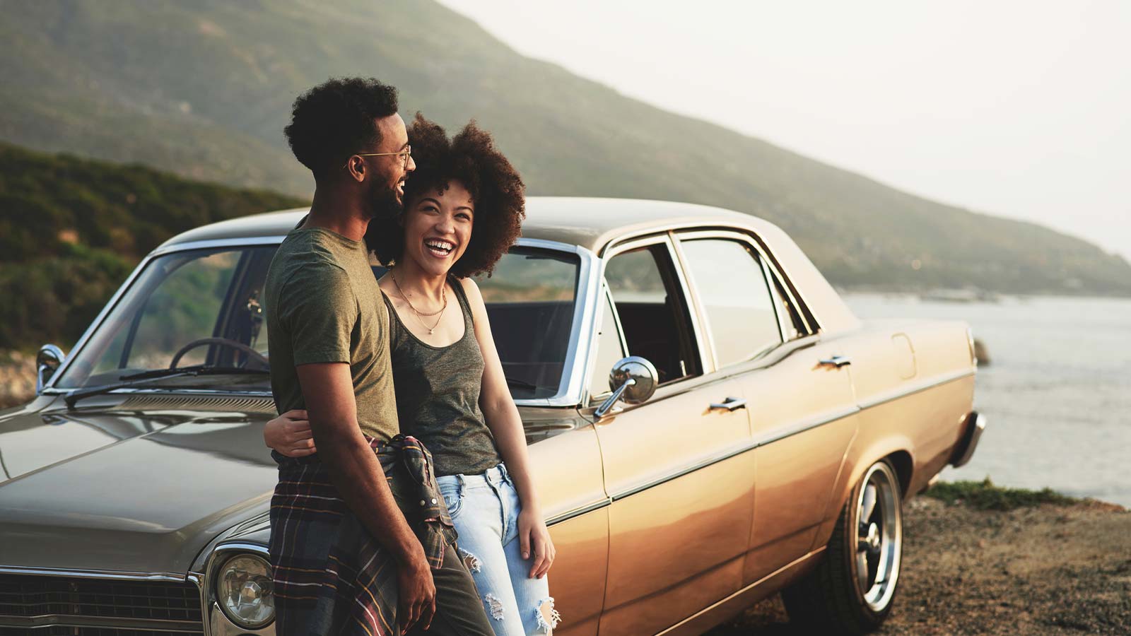 a happy couple standing outside of their car near the ocean